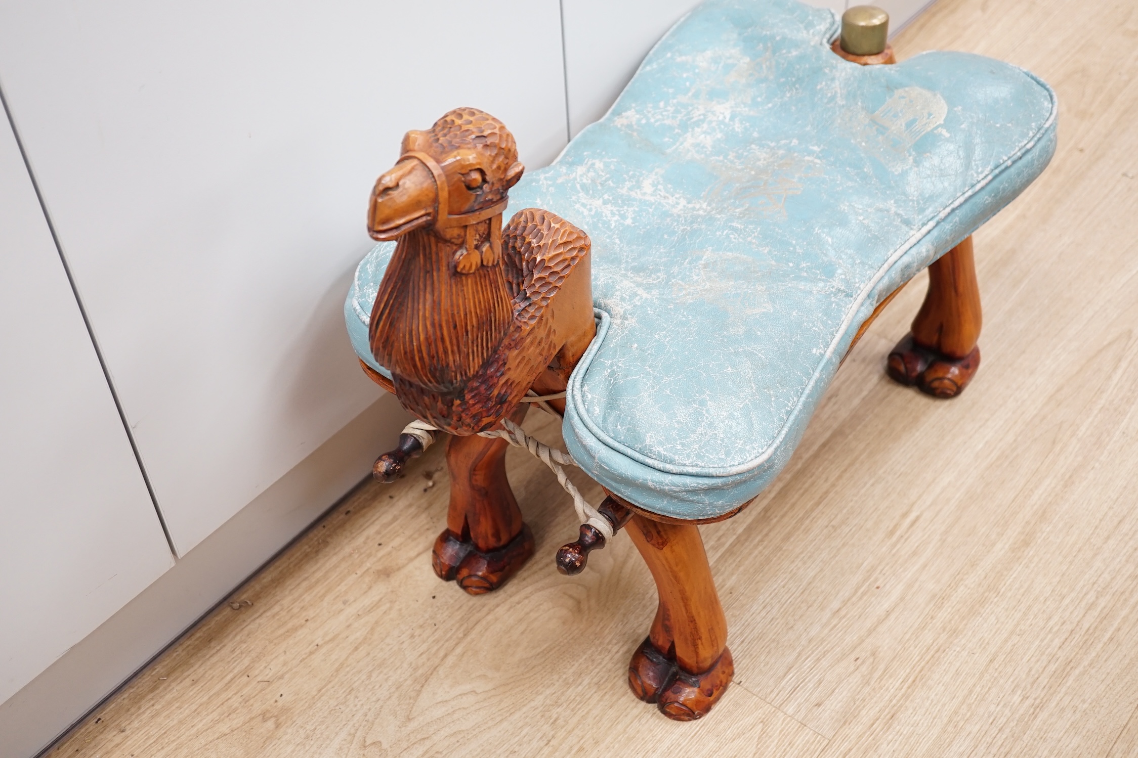 A carved wood foot stool in the form of a camel, blue stamped patterned leather cushion, 56cm high, 71cm wide. Condition - frame good, leather cushion worn